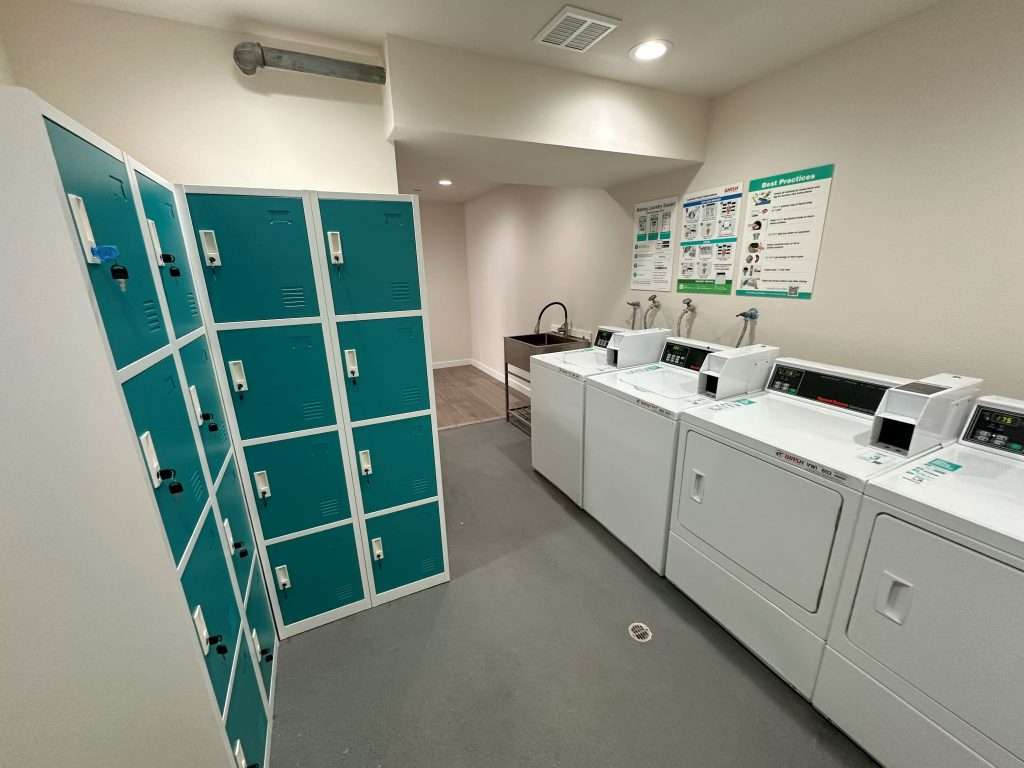 A laundry room with a utility sink, four washers and driers, and 4 columns of lockers in the adjacent corner.