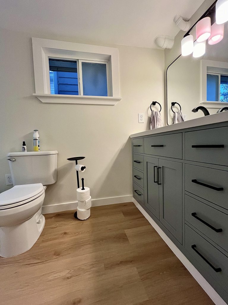 The entrance of the bathroom looks at a blue vanity, toilet, and small window.
