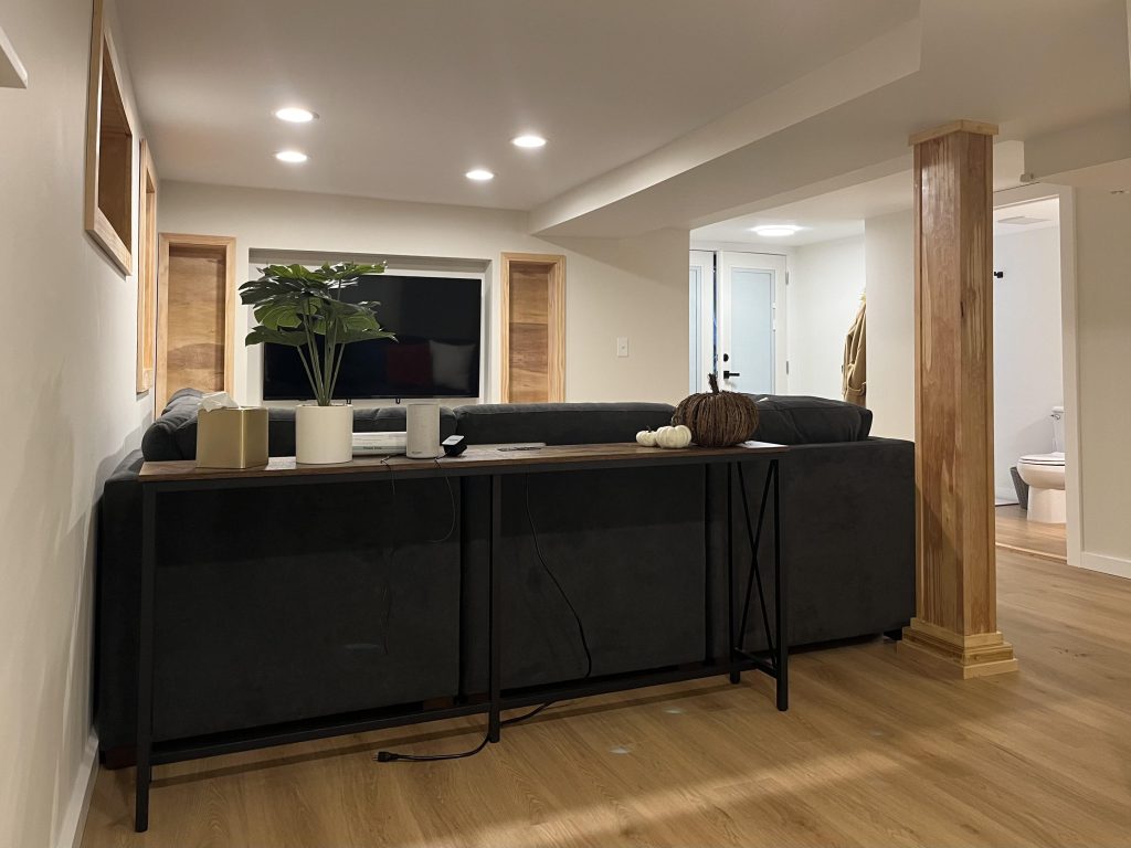 The view from the back corner of the living space in this basement conversion shows the built-in shelving, recessed lighting, and new laminate floors.