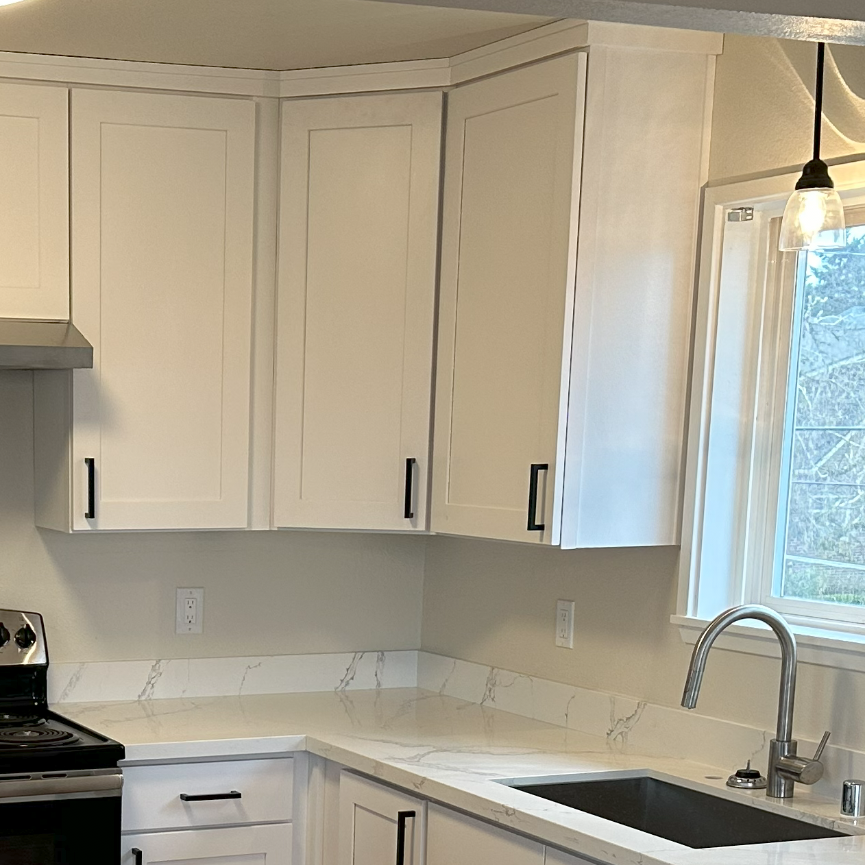 The small kitchen renovation features white cabinets and counters with stainless steel appliances.