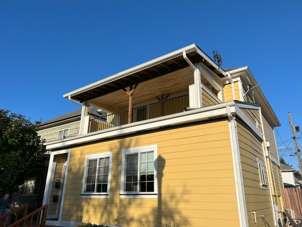 A covered second-story balcony with roof has a custom wooden ceiling, metal railing, and recessed lighting.