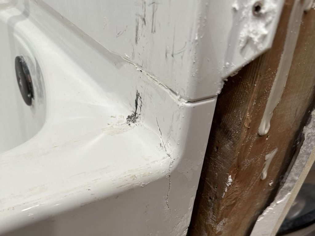A cracked bathtub basin and exposed framing show early signs of water damage.