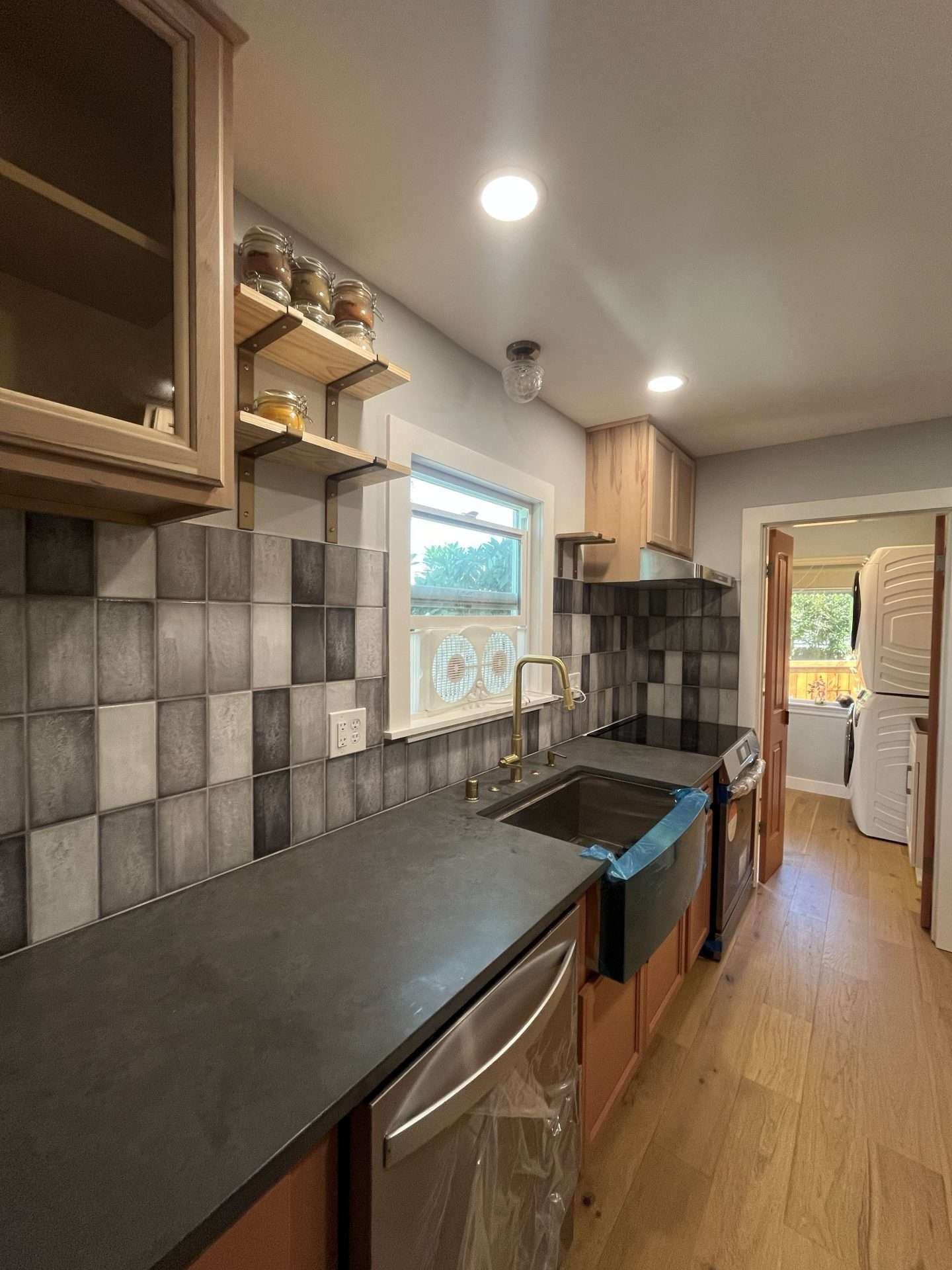 A newly remodeled kitchen with quartz countertops, a variegated gray tile backsplash, and custom.cabinetry and floating shelves.
