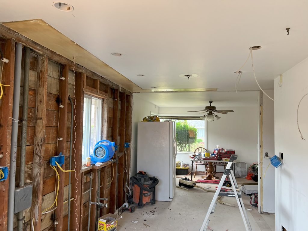 A demoed kitchen has all cabinets and counters removed and is missing the wall that previously separated the kitchen from the dining space.
