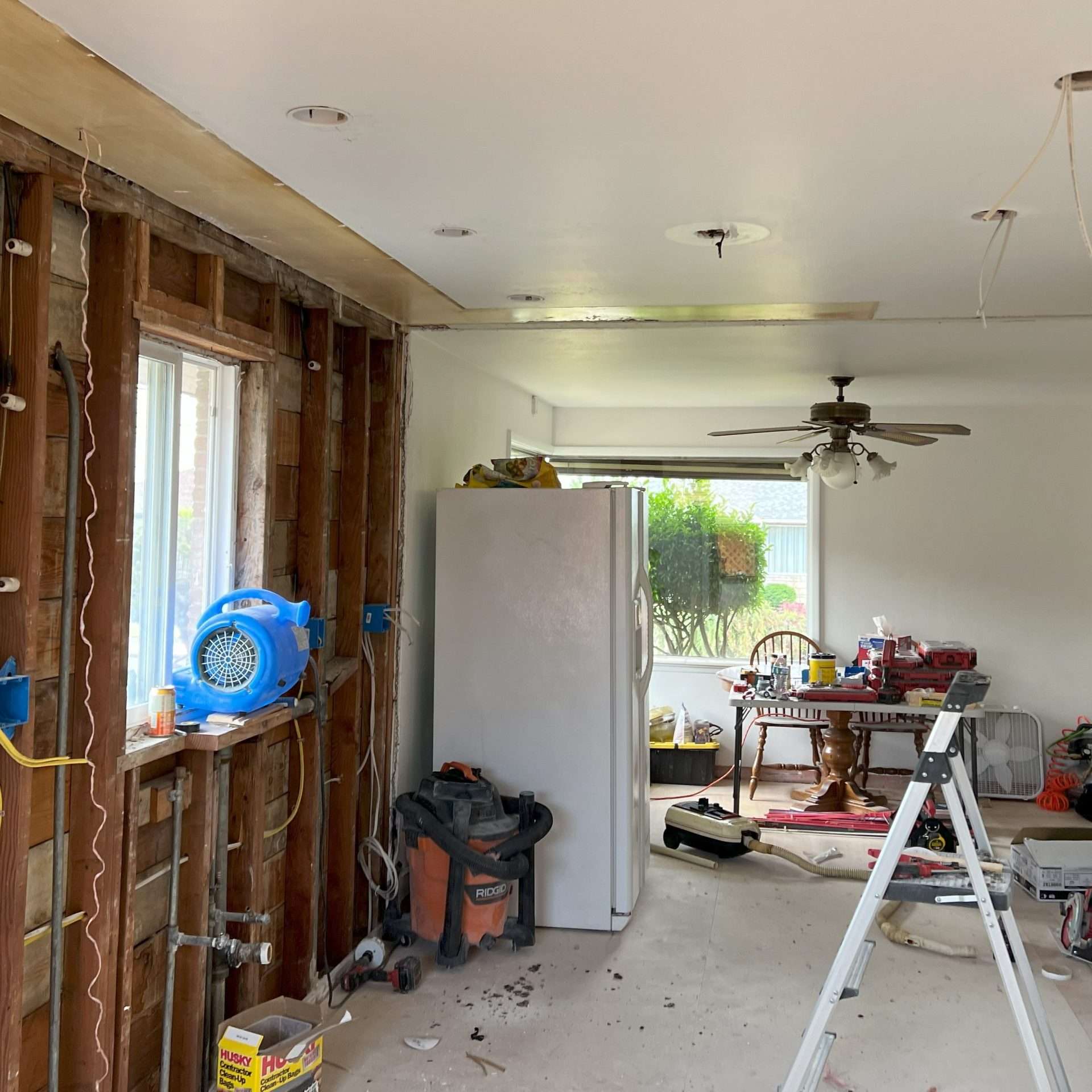 A demoed kitchen has all cabinets and counters removed and is missing the wall that previously separated the kitchen from the dining space.