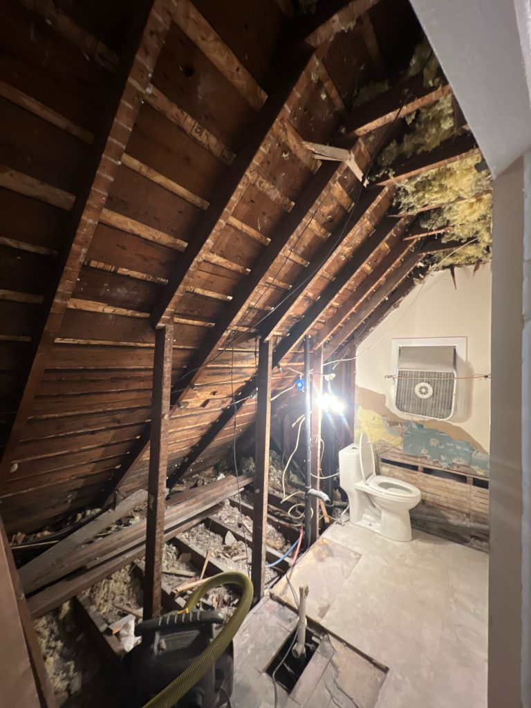 A small bathroom remodel with the tub and wall removed exposes the space under a slanted roof.