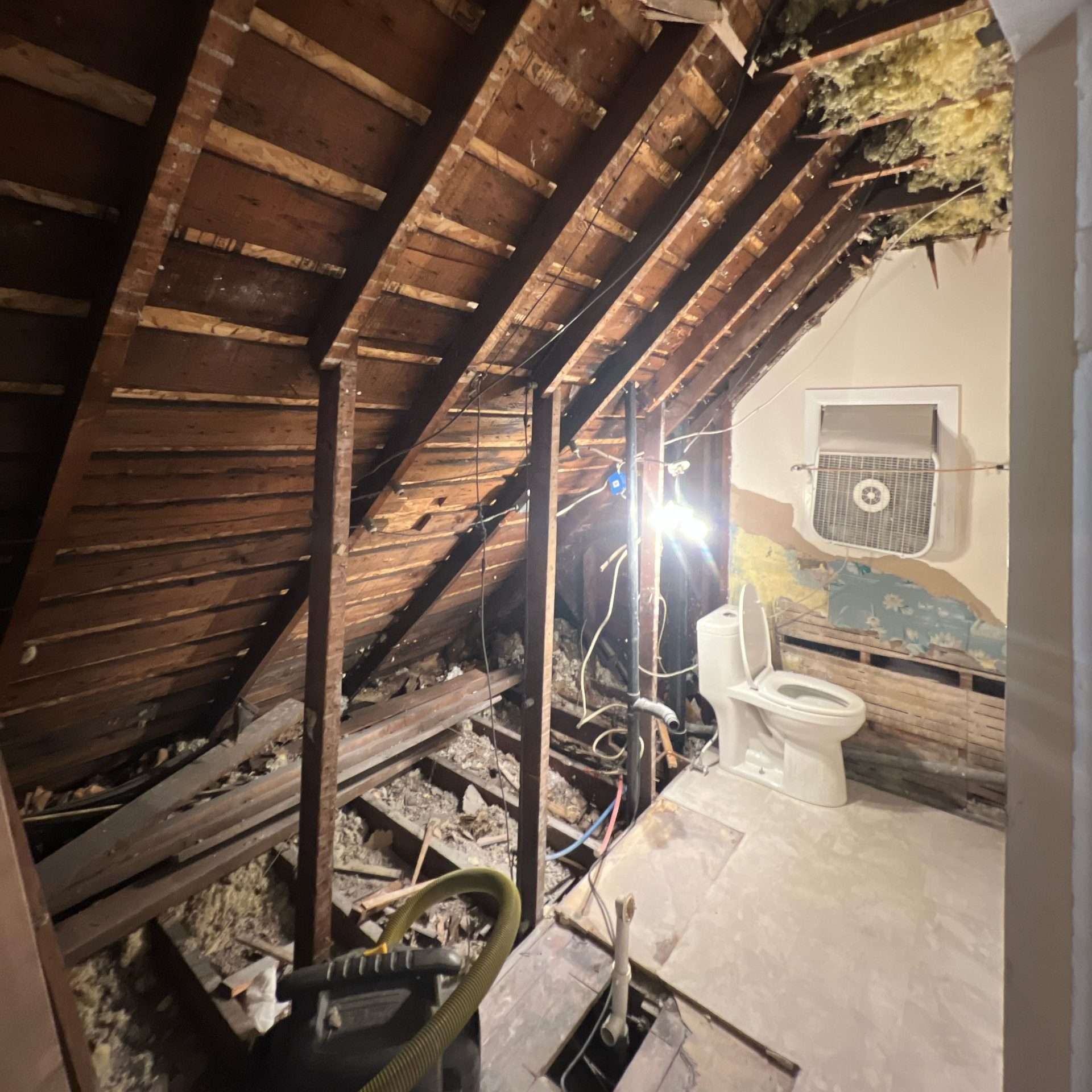 A small bathroom remodel with the tub and wall removed exposes the space under a slanted roof.