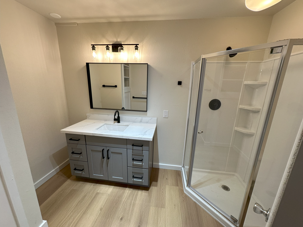 A master bathroom with a corner shower, vanity, and wide mirror.