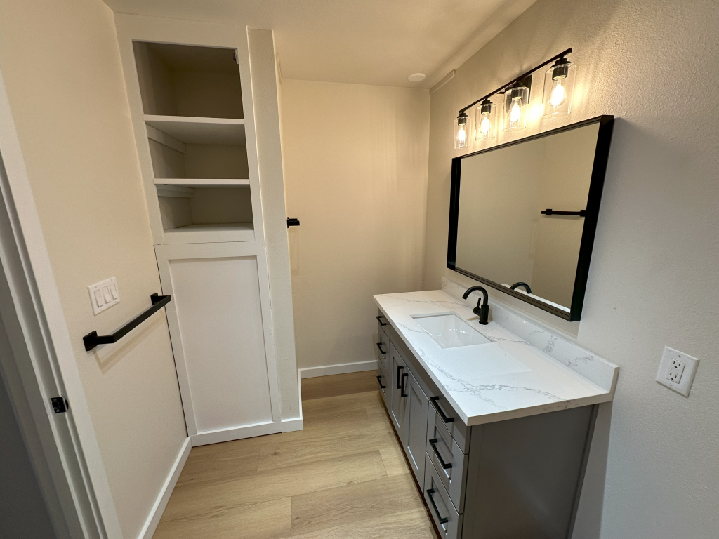 A bathroom with a vanity, towel rack, and corner storage.