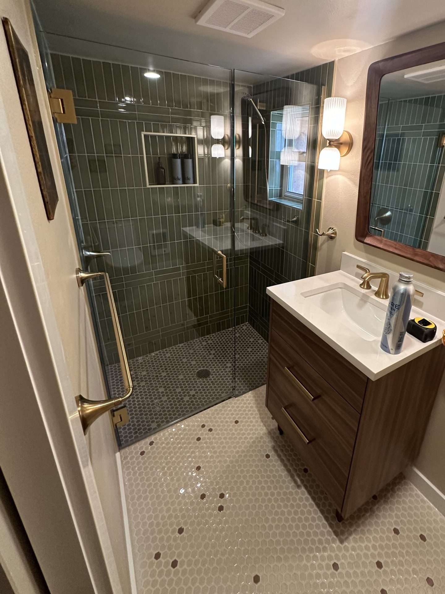Finished basement bathroom with wood vanity, framed mirror, glass shower enclosure, and green tile walls.