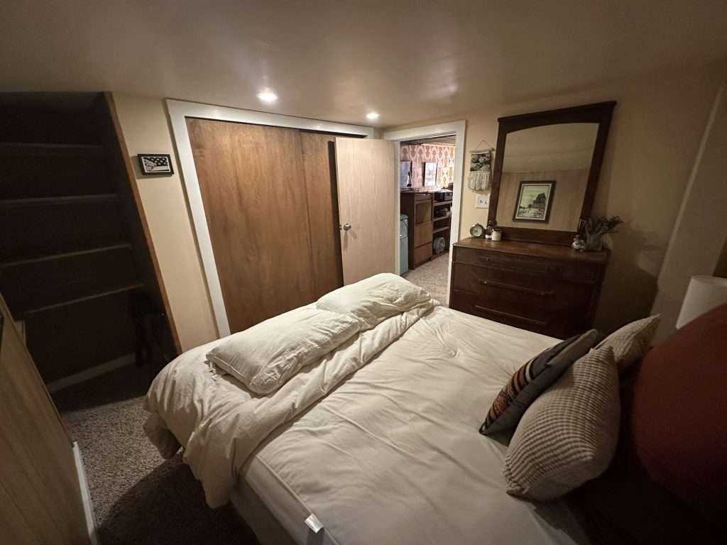 Finished basement bedroom with sliding closet doors, carpet flooring, and dark wood furniture.
