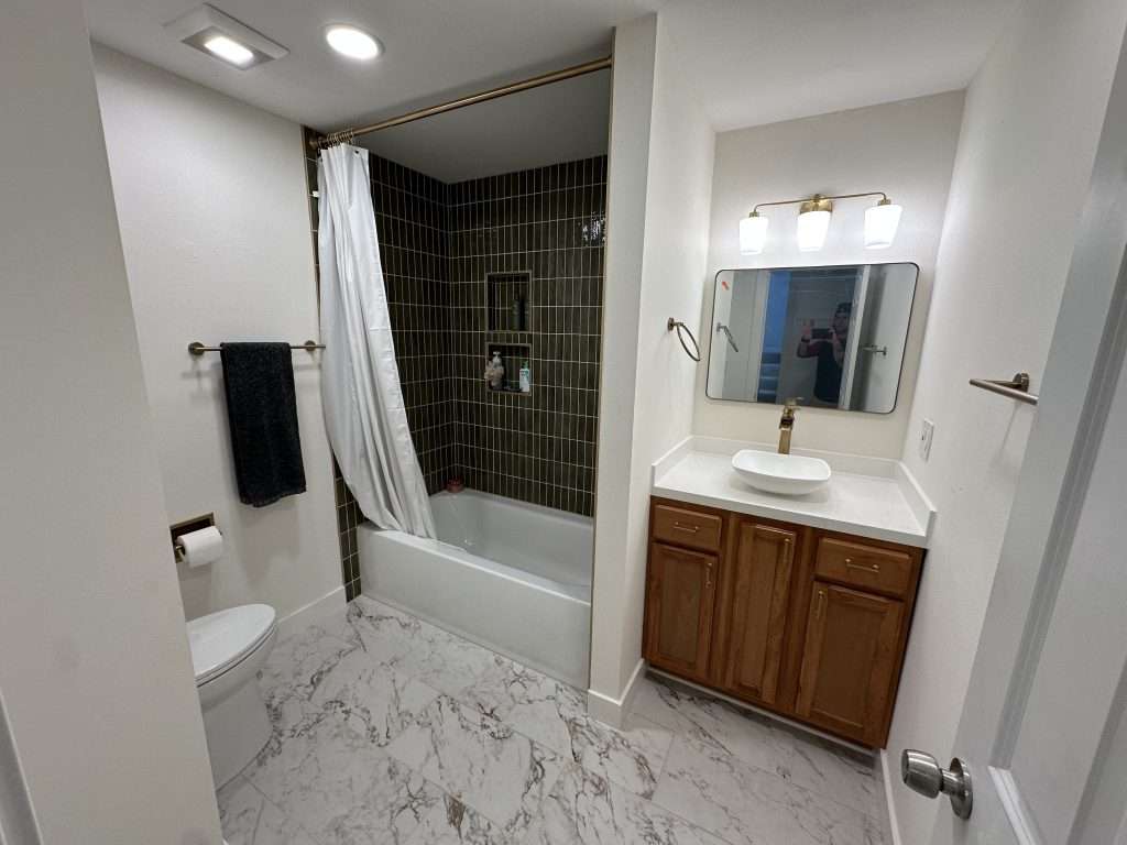 A modern bathroom with green tile accents and marble-look floors.