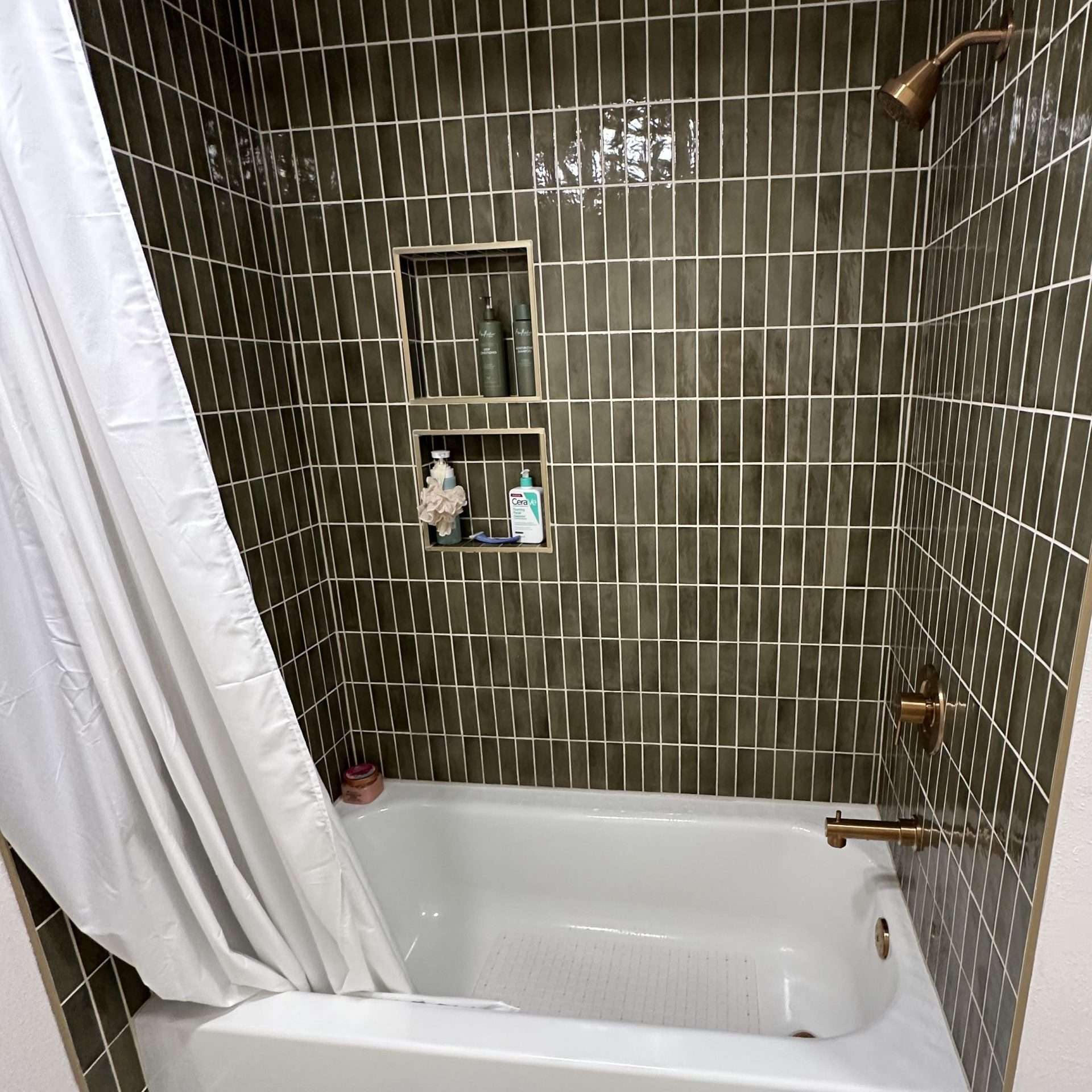 Modern bathtub with green tiled walls, a storage nook, and marble floors.