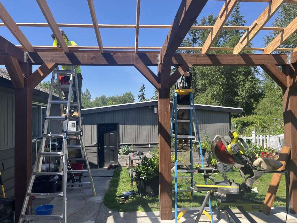 Two contractors on ladders assempling the roof framing of a custom patio cover.