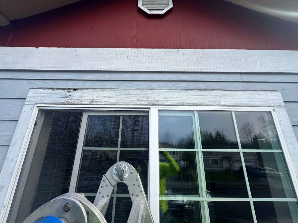 Peeling paint, cracking caulk, and rotted trim around the exterior of a second-story window.