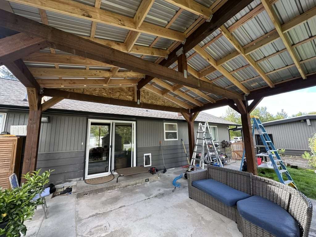A completed view of a custom wood patio cover with a metal roof and outdoor furniture beneath.