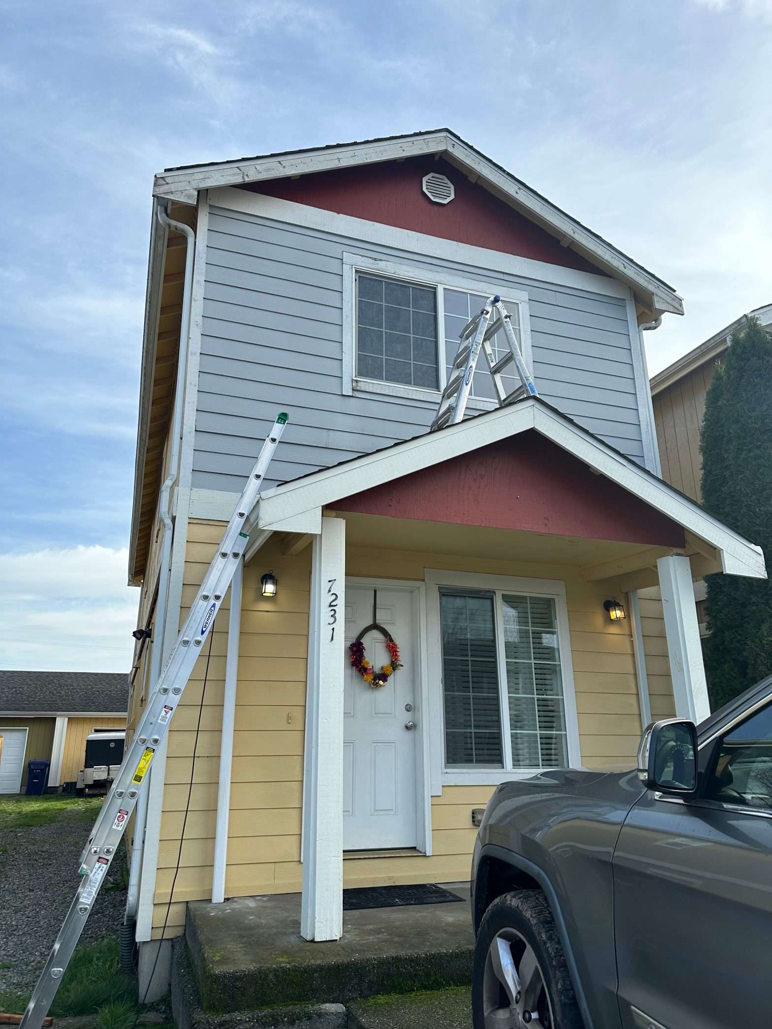 The front of a two story home with two ladders set to reach the second story window.