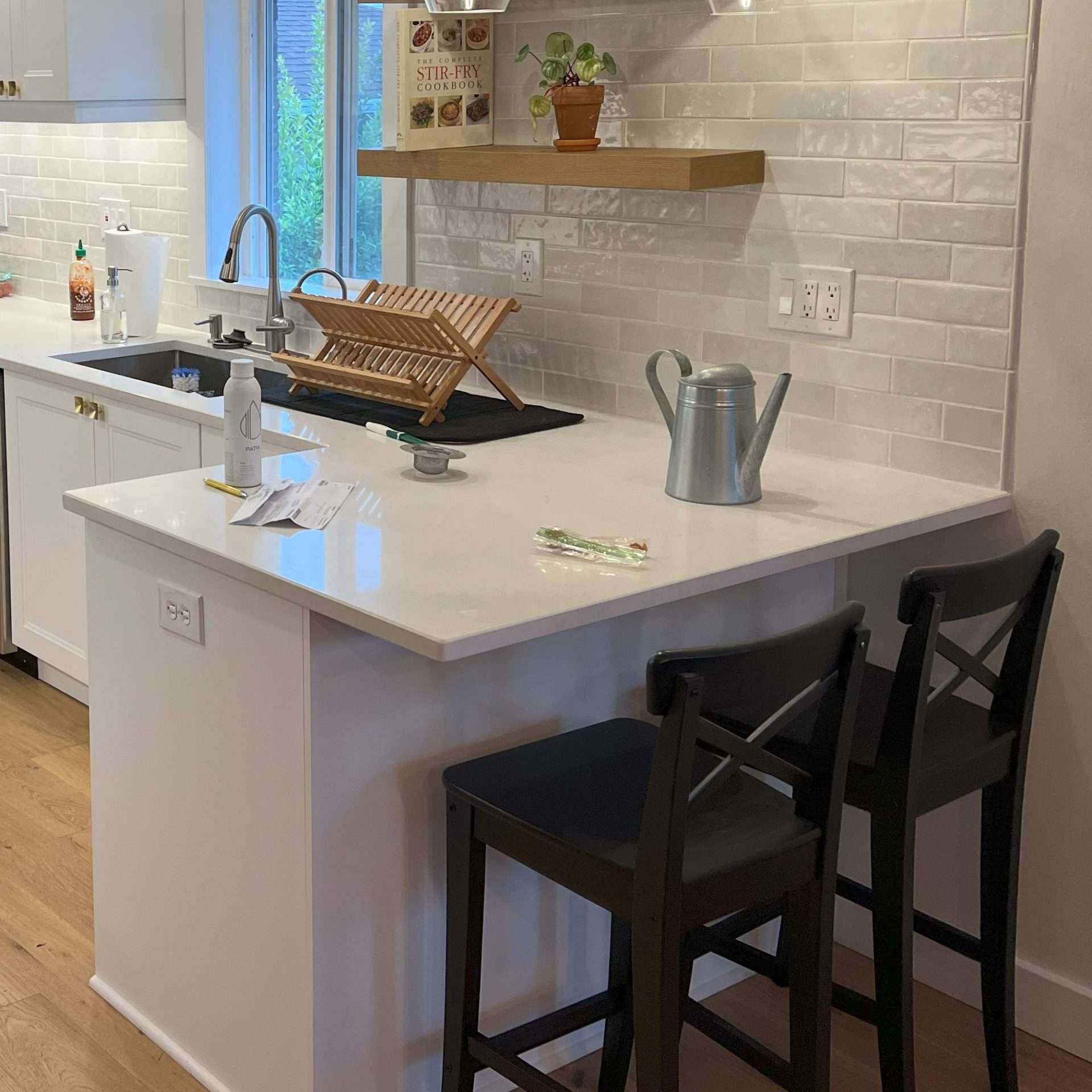 A modern kitchen remodel includes white cabinets, counters, and tiling, as well as bar seating and floating shelves.