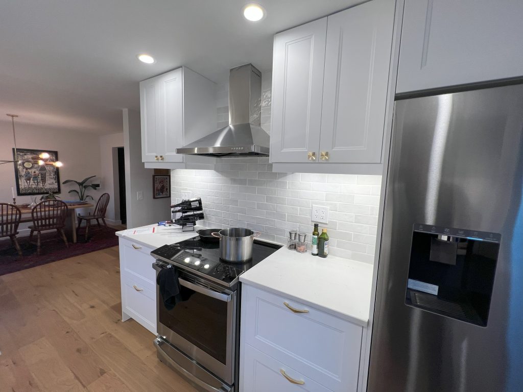 A Seattle kitchen remodel features light wood floors, white counters and cupboards, and stainless steel appliances.