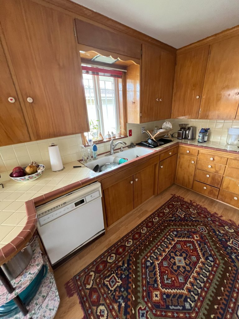 A mid-century-style kitchen with laminate countertops, wood cupboards, and white sinks and appliances.