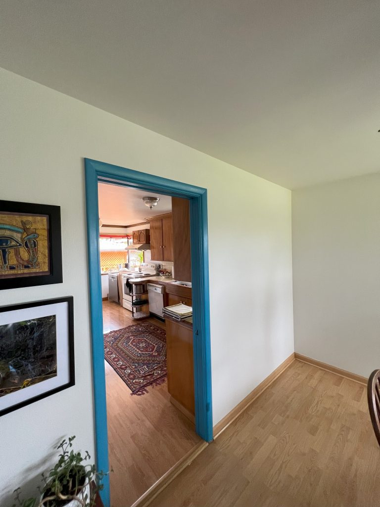 A beige wall with a wide-open passage in the middle separates the kitchen from the adjacent room.