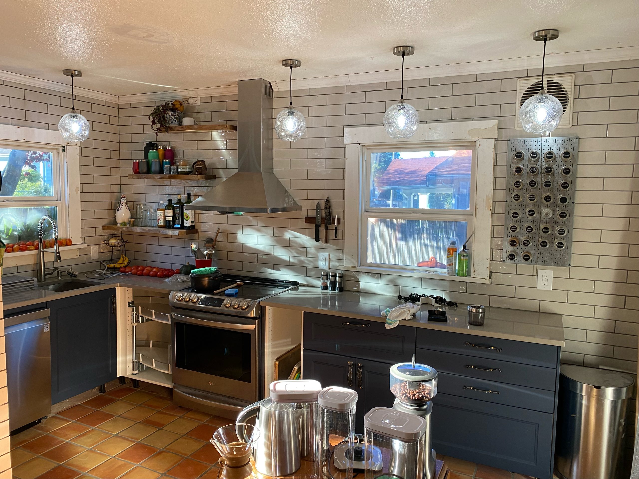 A small kitchen with white subway tiles, blue cabinets, and decorative pendant lighting has a creative, yet industrial ambiance.