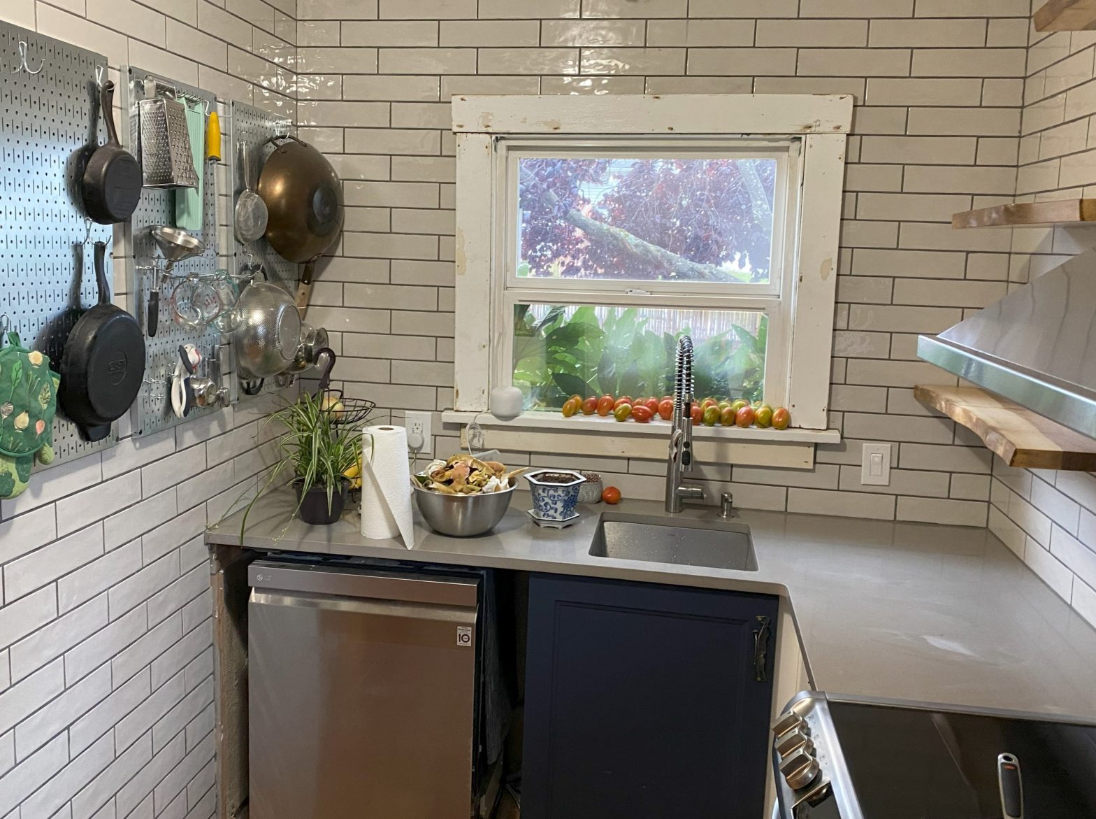 A kitchen nook features a wall-mounted pan rack, dishwasher, stove with oven, floating shelves, and a small window.