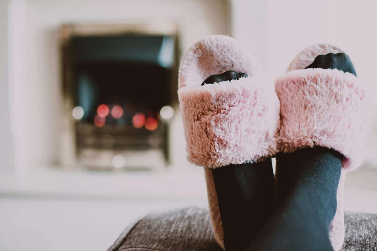 A pair of feet are propped up with fuzzy pink slippers on while the fireplace burns in the background.
