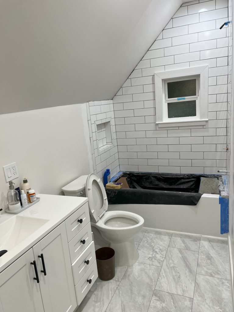 A nearly-completed small bathroom remodel features marble floor tiles and subway tiling around the tub.