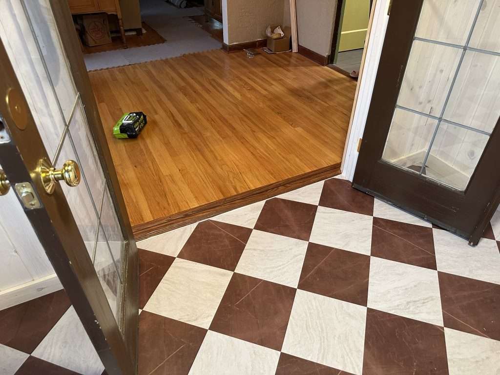 The checkerboard floor of a sunroom extension transitions smoothly into the kitchen through glass french doors.