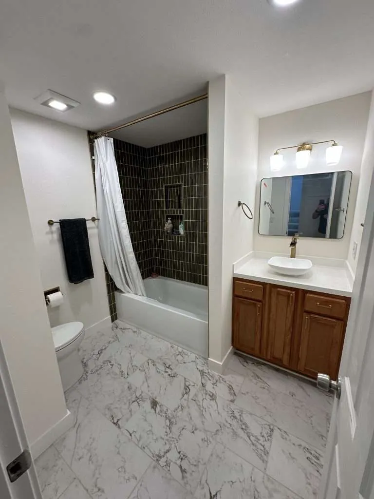tiled bathtub surround with marble floor and vessel sink