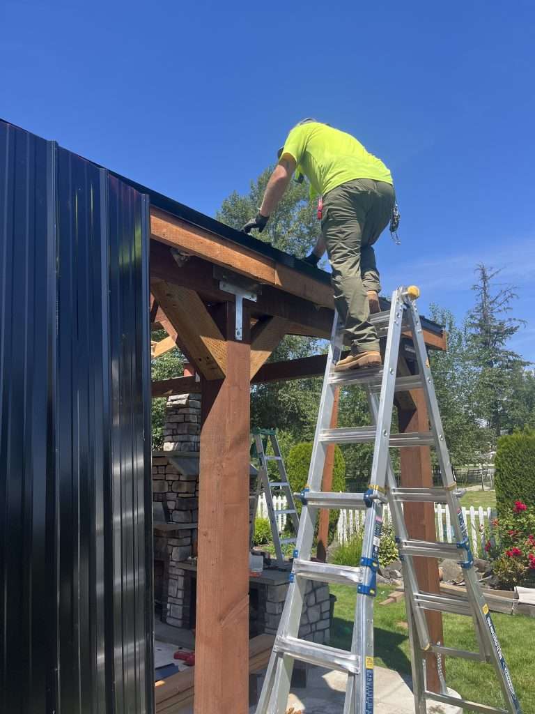 A contractor on a ladder fastening a metal roof to the framing.