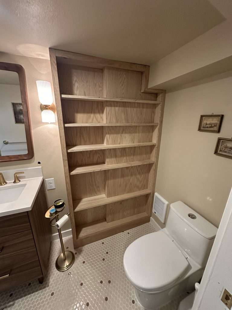 Wide view of custom bathroom shelving, toilet area, and built-in storage with natural wood cabinetry.